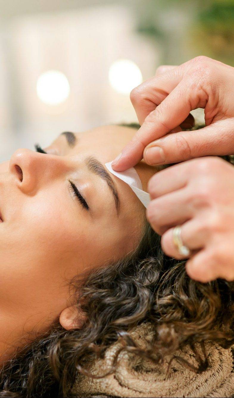 Master waxing eyebrow of relaxed client in beauty studio